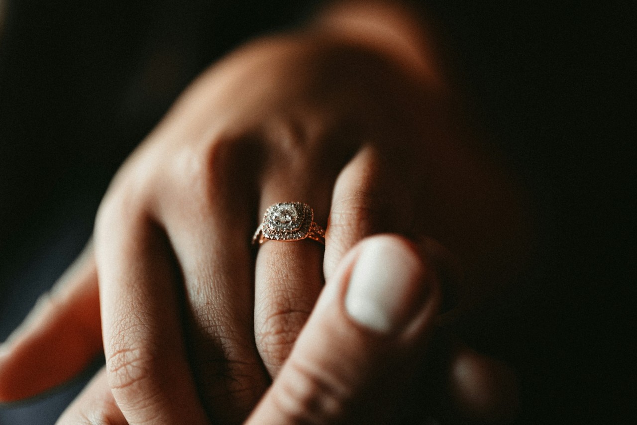 a man’s hand holding a woman’s that is adorned with a double halo diamond engagement ring