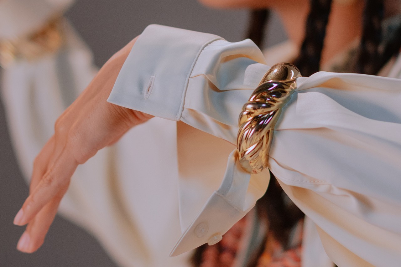 A close-up image of a woman’s wrist adorned with a chunky yellow gold, textured cuff bracelet