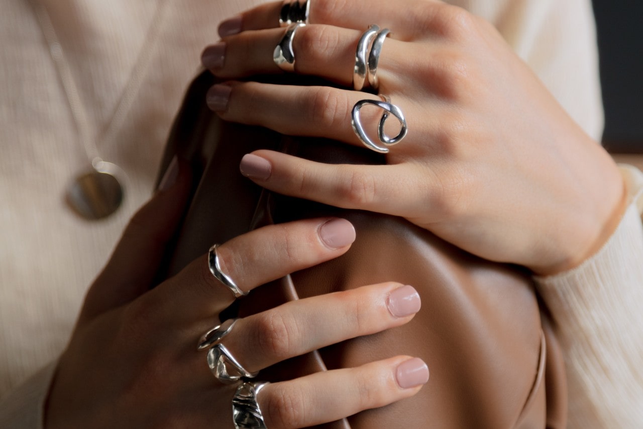 A close-up image of a woman’s hands, wearing sculptural fashion rings.