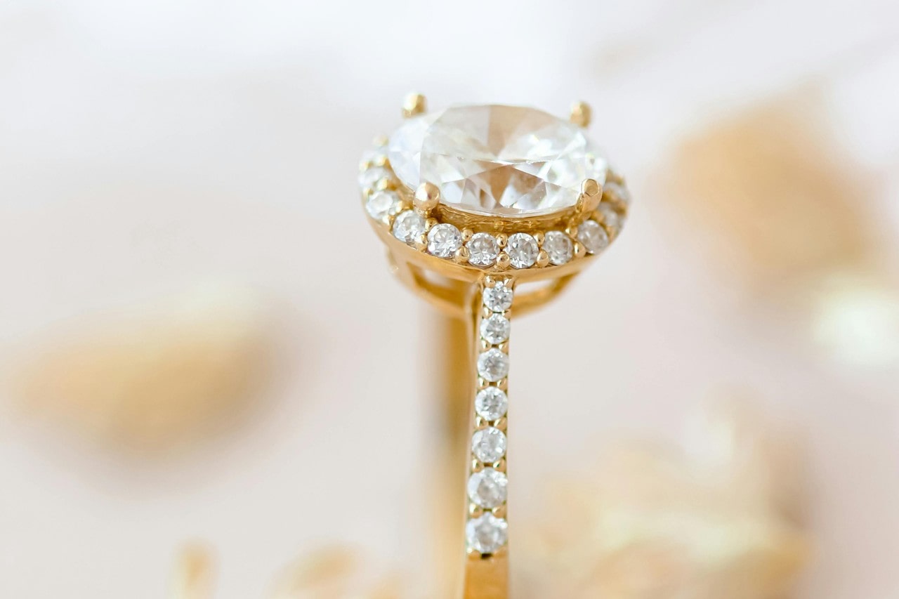 close up image of a yellow gold engagement ring with an oval cut center stone, halo, and side stones