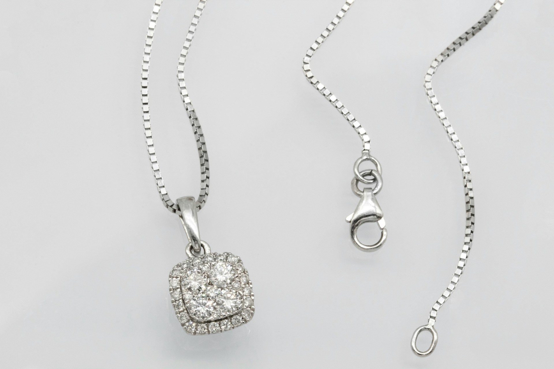 a white gold necklace with a diamond pendant on a gray surface