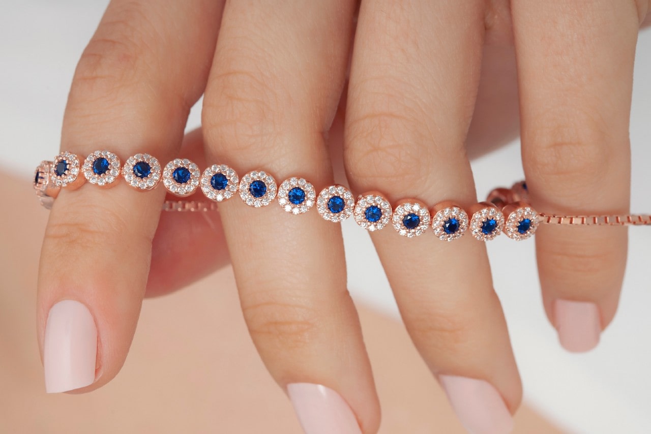 a woman’s hand holding a rose gold bracelet with sapphires and diamond accents
