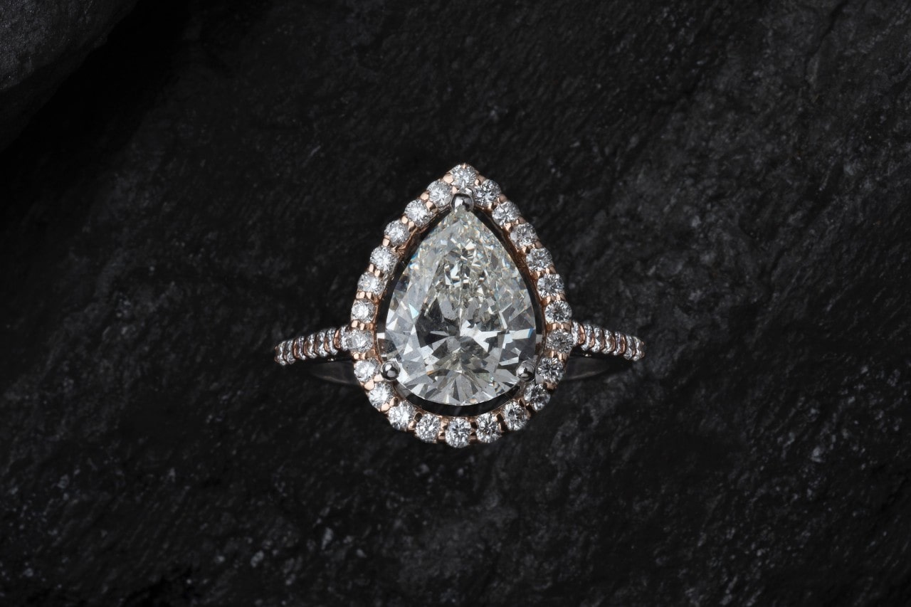 a pear shape halo engagement ring on a dark stone background