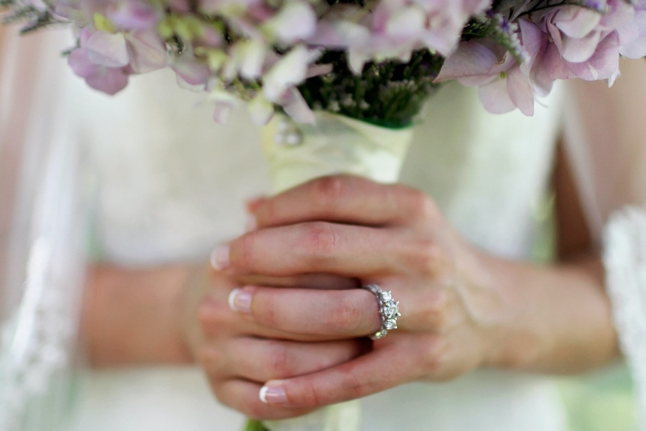 lady’s hands wearing an engagement ring and holding flowers