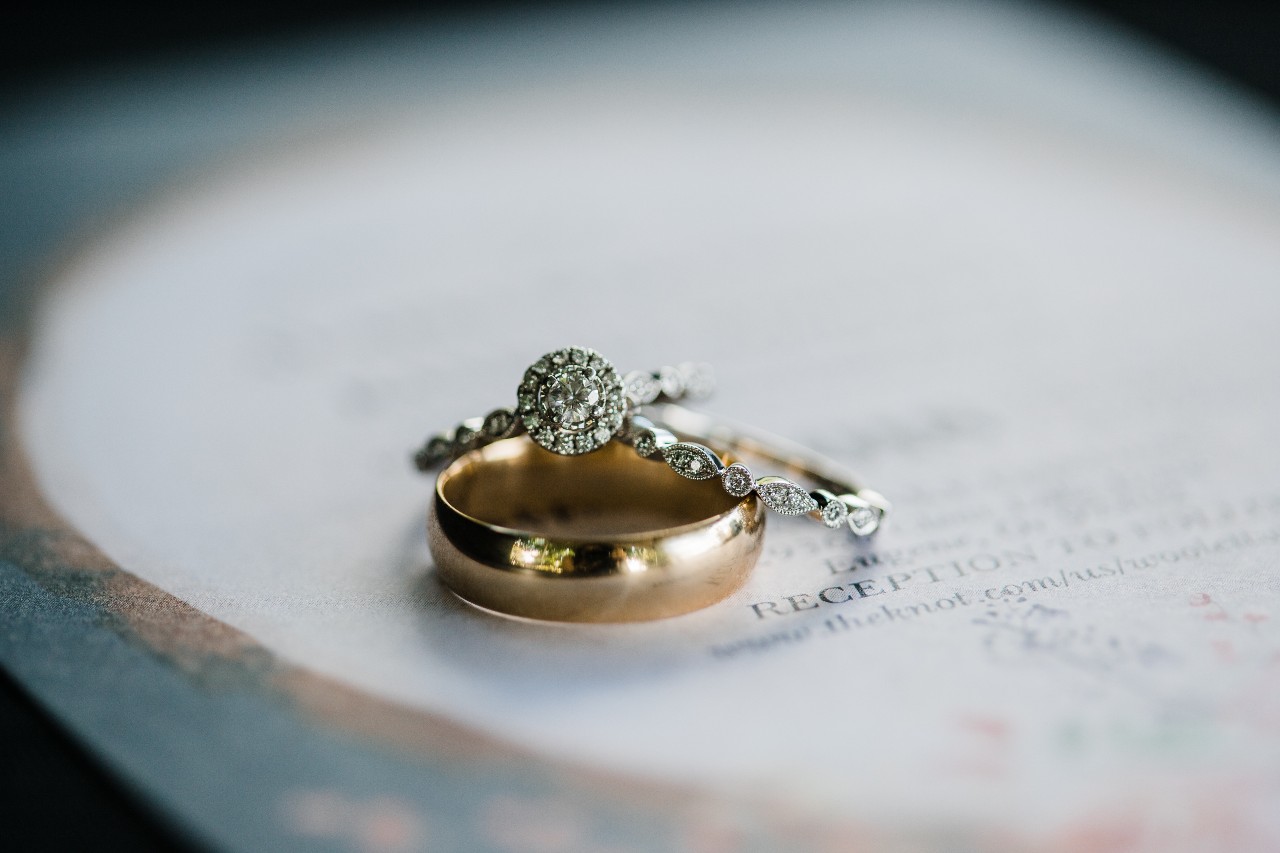 a halo engagement ring sits with 2 wedding bands on an invitation.