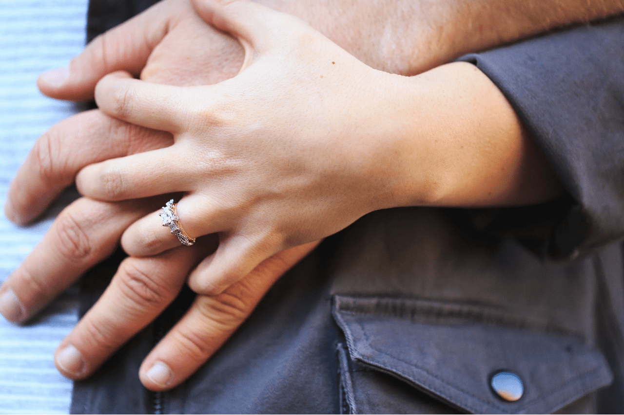 a close-up of a couple holding hands, the woman wearing a three-stone ring.