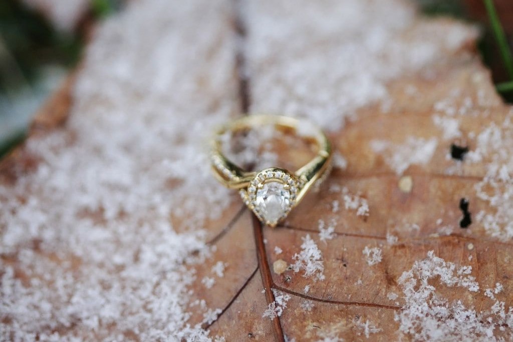 a gold pear-shaped engagement ring sits on a frosted leaf.