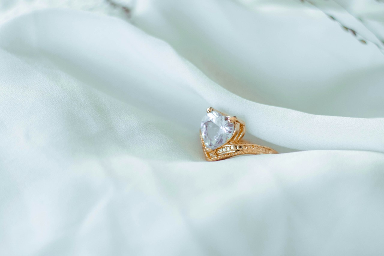 a yellow gold engagement ring with a heart shaped diamond center stone on a white sheet