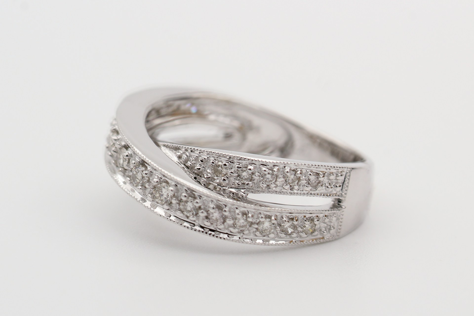 a white gold fashion ring featuring overlapping bands and diamond accents