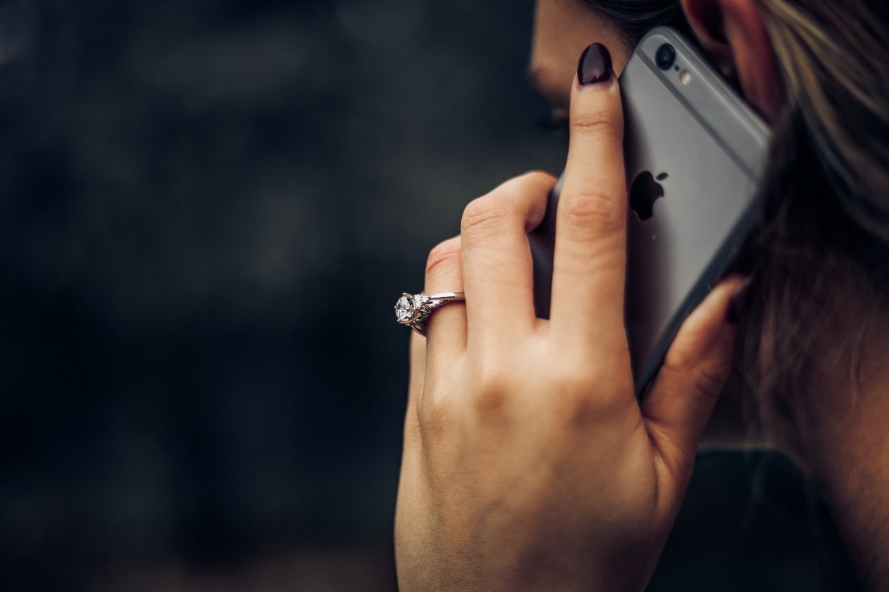 A woman talking on her iPhone, a white gold engagement ring prominently visible on her finger.