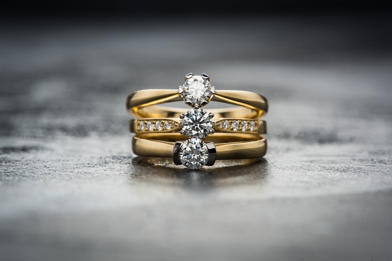 Three yellow gold engagement rings in different styles lay on a stone surface.