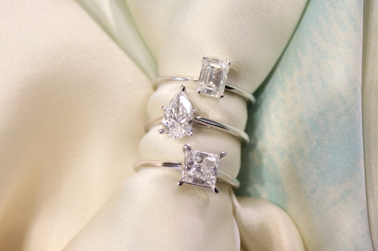 A close-up of three diamond engagement rings displayed on a beige cloth napkin.