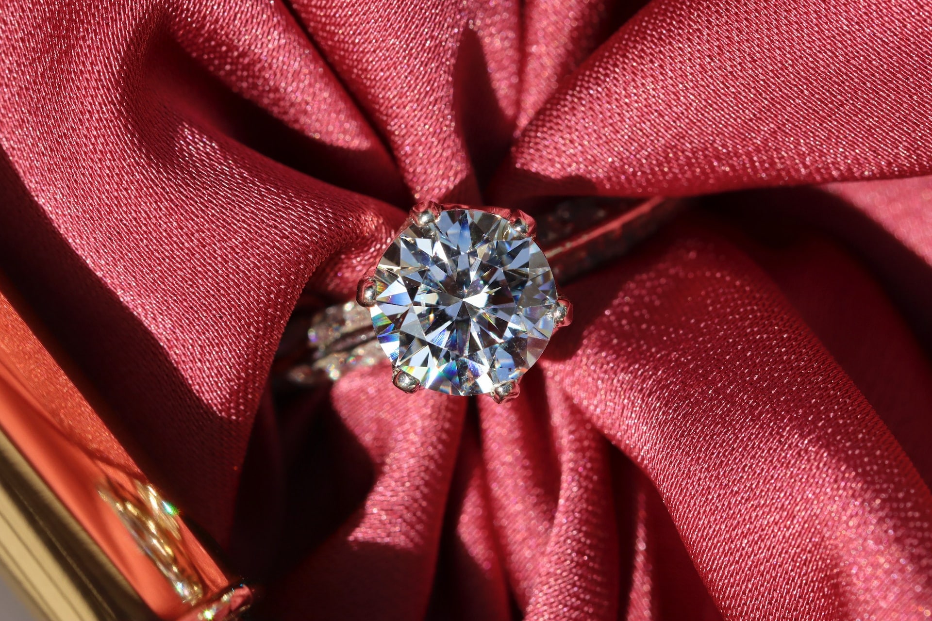 A close-up of a solitaire diamond ring displayed on a piece of textured red fabric.