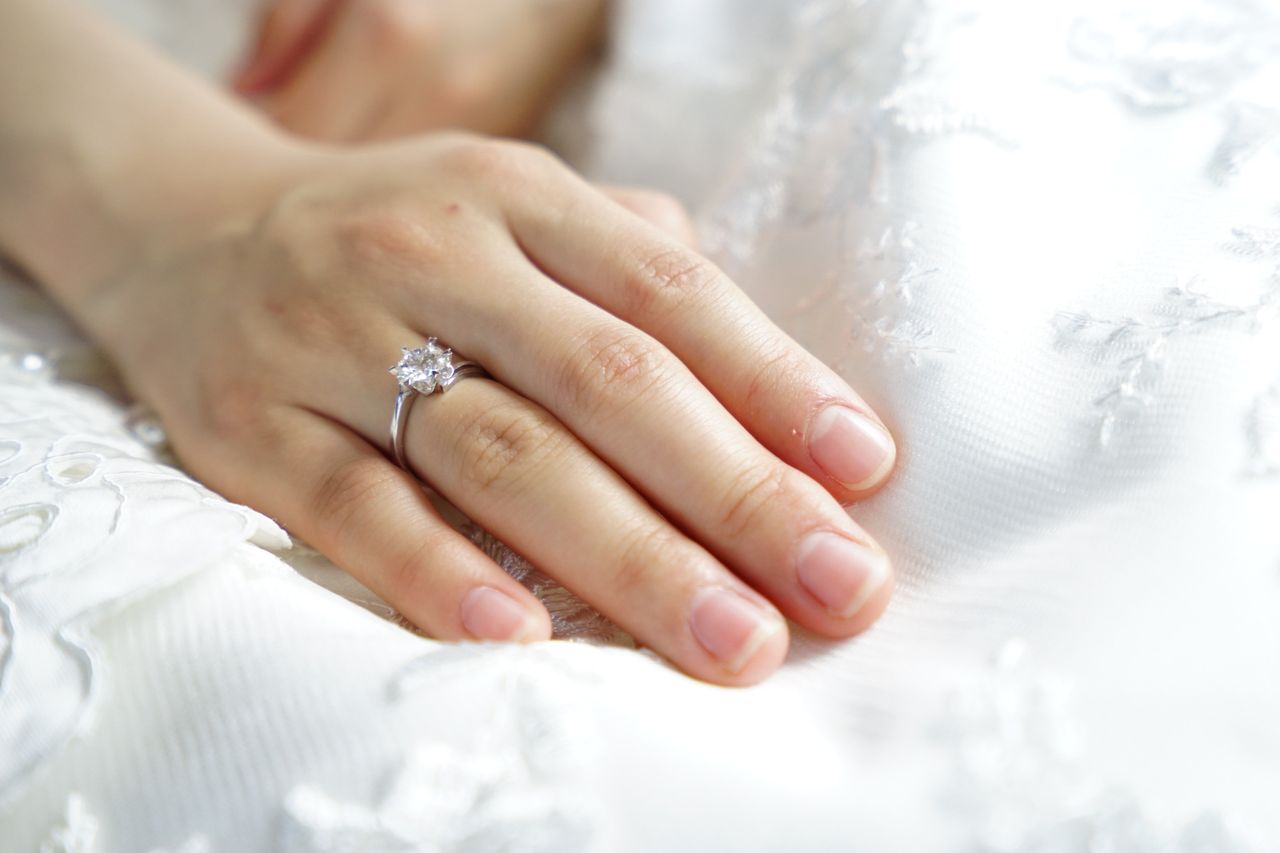 A close-up of a bride’s hand atop her wedding dress, adorned with a solitaire engagement ring.