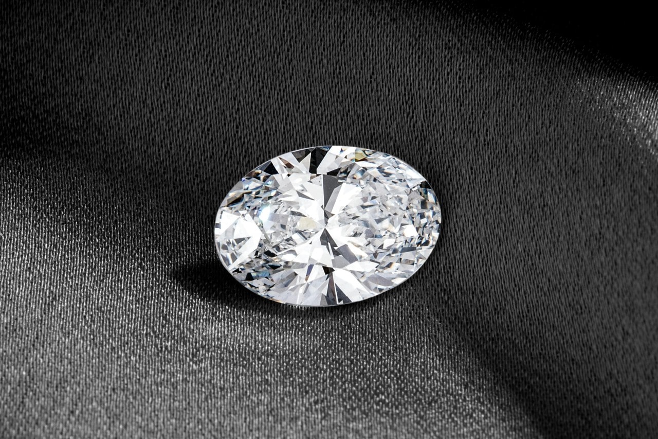 A close-up of a sparkling oval-cut diamond on a dark fabric background.