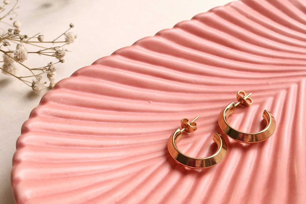 a pair of yellow gold huggie earrings lying on a pink dish