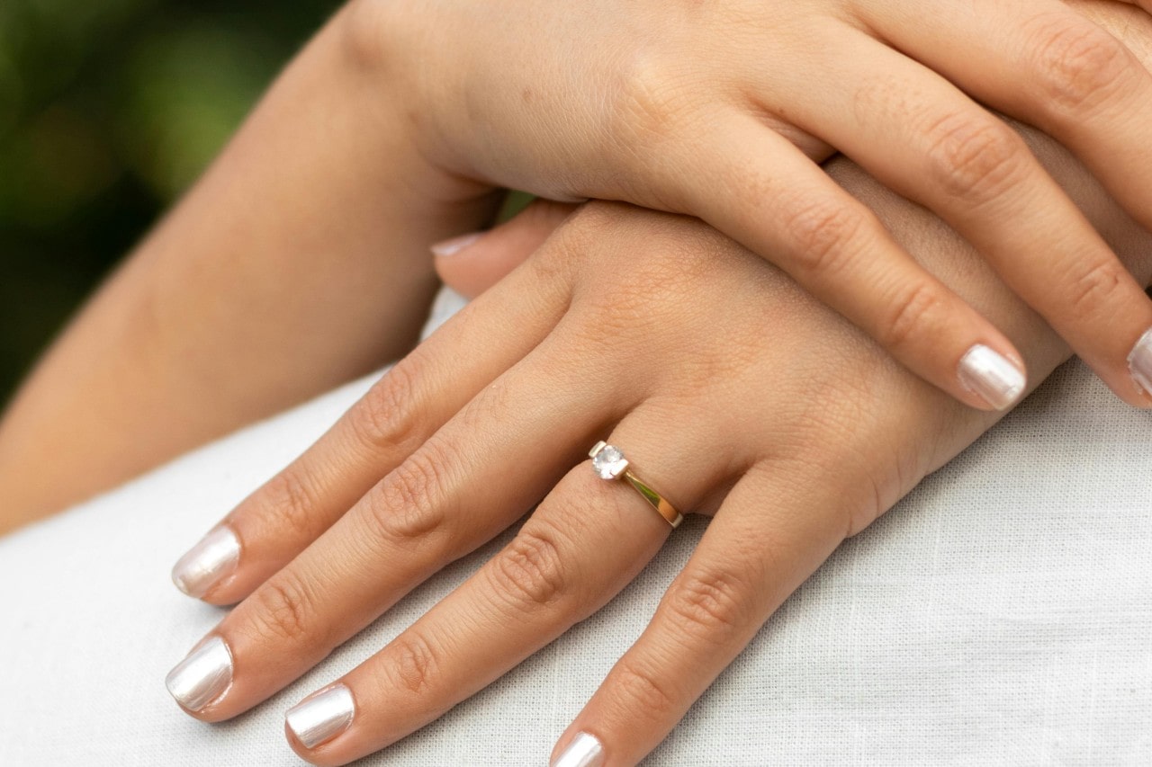 a woman’s hands wearing a solitaire, yellow gold engagement ring