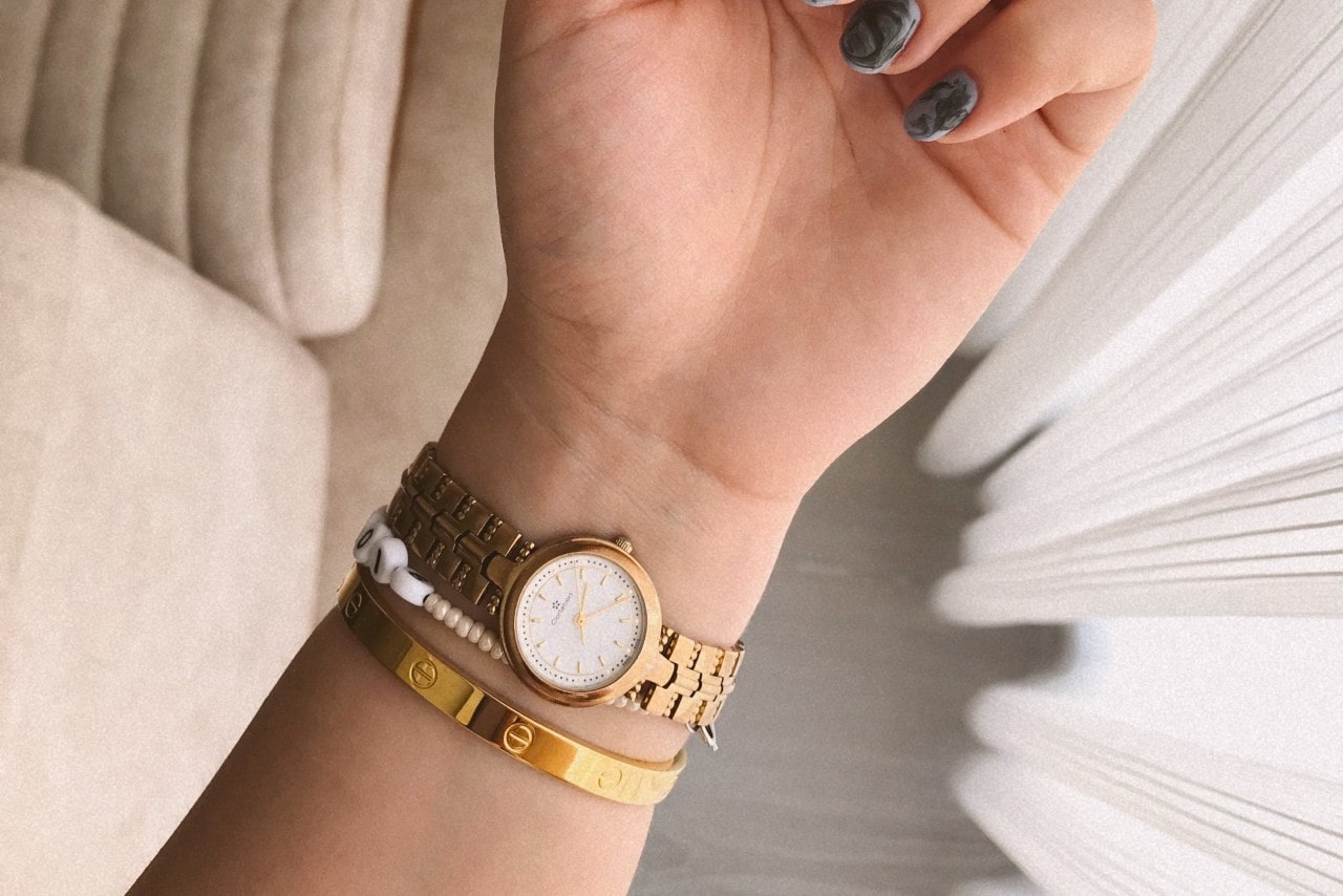 a woman’s wrist displaying a yellow gold watch and two bracelets